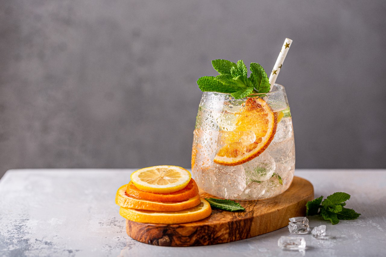 Fresh cocktail with crushed ice, mint leaves and divers oranges on the gray table.