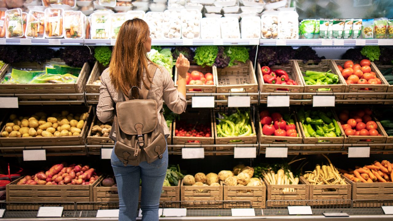 Good looking woman standing in front of vegetable shelves choosing what to buy.