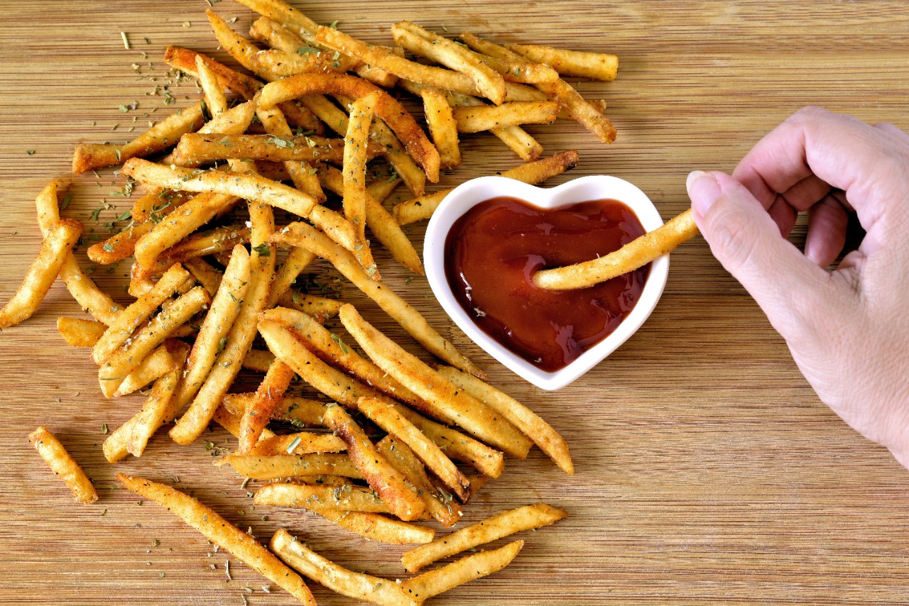 Dipping French fries in a heart shaped bowl of ketchup